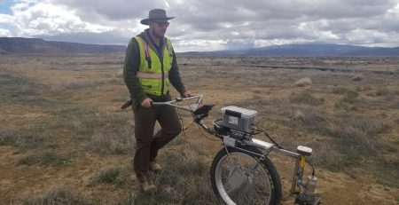Person using a metal detector in an open field under cloudy skies.
