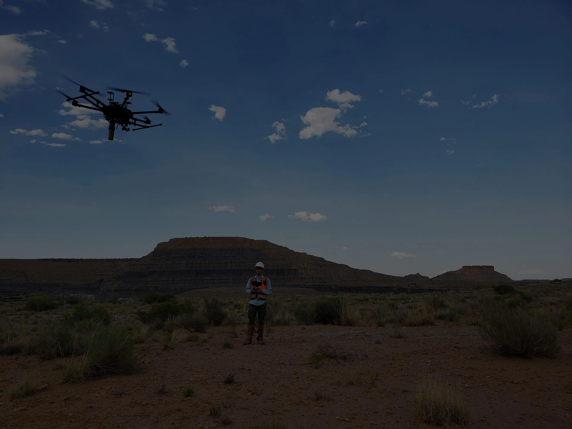A drone flies over a desert landscape with a person controlling it.